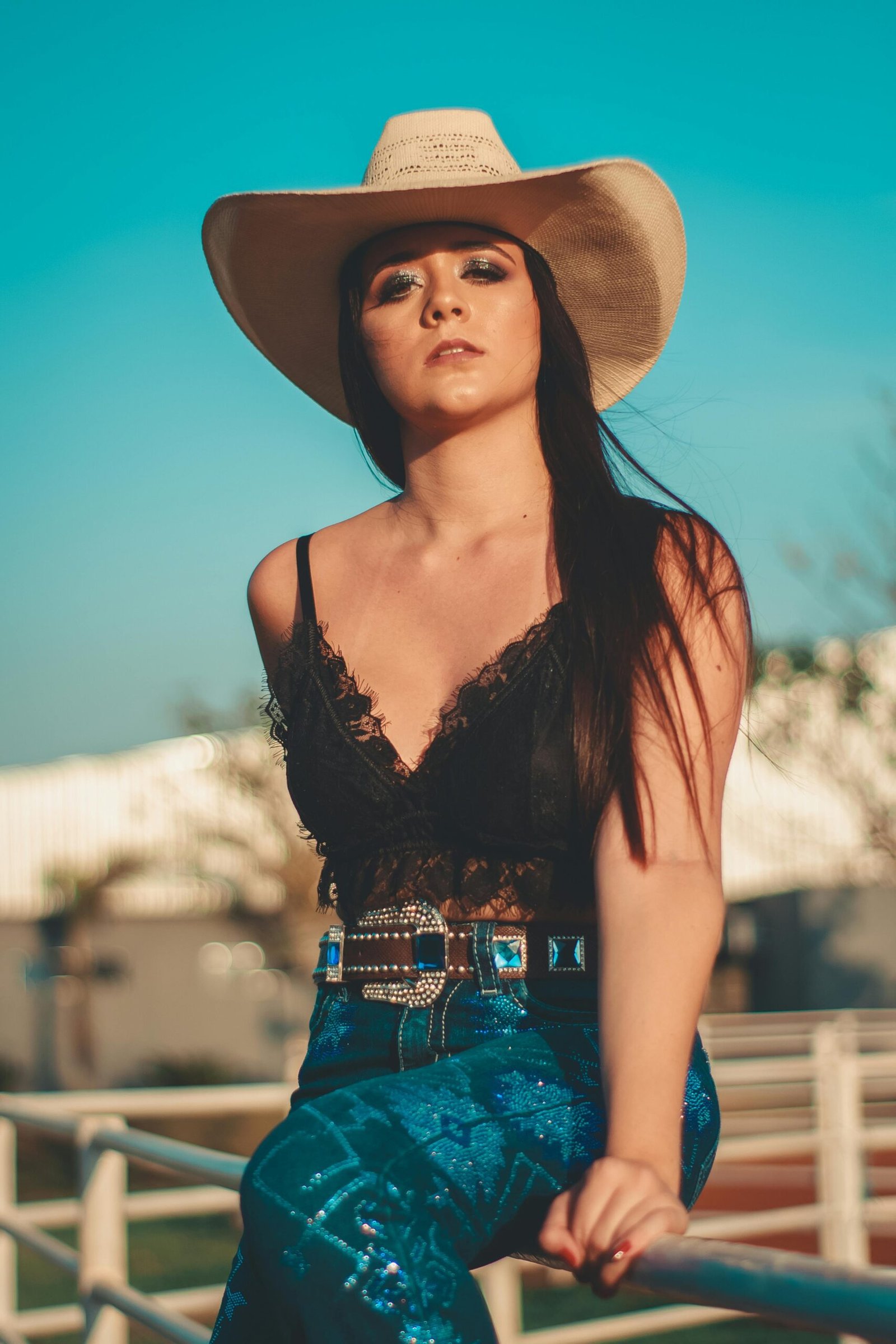 A fashionable woman in Western attire poses confidently outdoors under a bright blue sky.