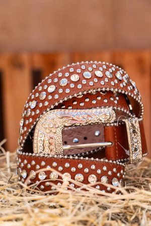 Close-up of a stylish western belt adorned with studs and a decorative buckle, set on straw.